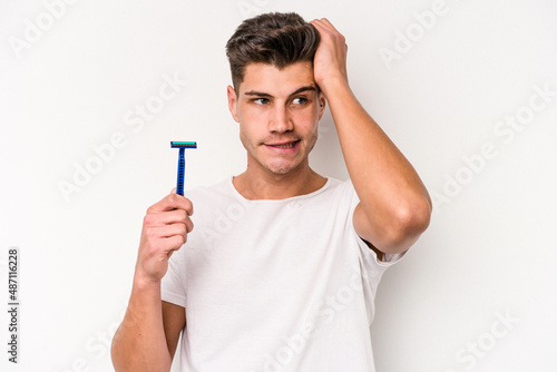Young caucasian man shaving his beard isolated on white background being shocked, she has remembered important meeting.