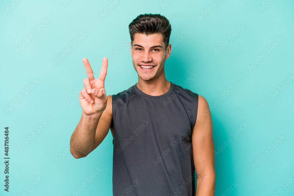 Young caucasian man isolated on blue background showing victory sign and smiling broadly. Young caucasian man isolated on blue background showing victory sign and smiling broadly.