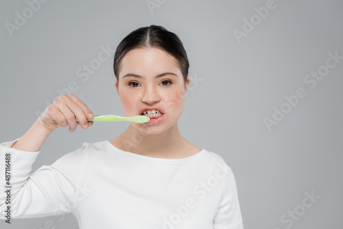 Woman with down syndrome brushing teeth isolated on grey