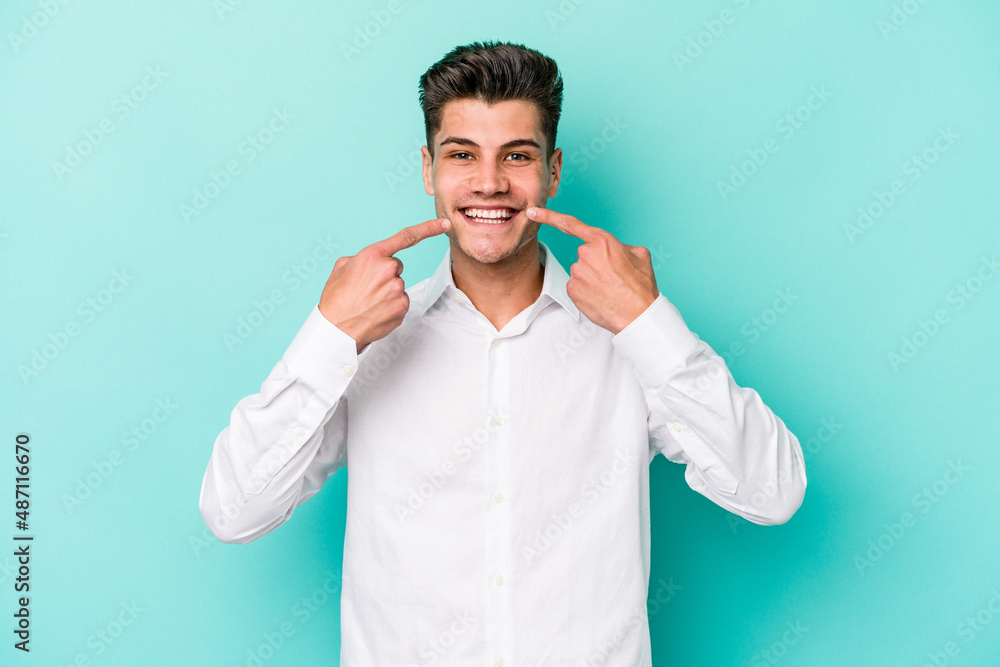 Young caucasian man isolated on blue background smiles, pointing fingers at mouth. Young caucasian man isolated on blue background smiles, pointing fingers at mouth.