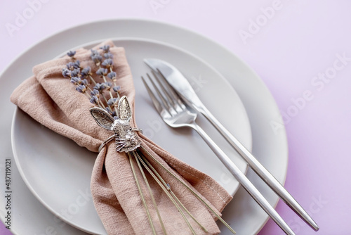 Banner. Table setting. A plate with a rabbit on a napkin, lavender and Easter eggs on a fashionable background of 2022 is a veri pery. Top view. The concept of a happy Easter holiday for cafes. photo