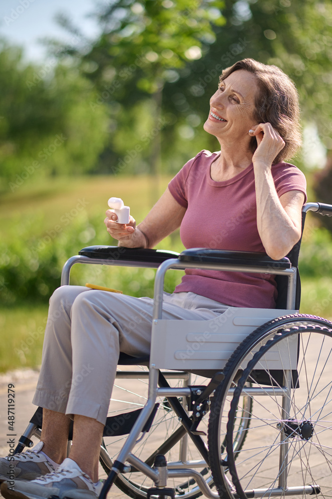 A smiling woman on a wheel-chair putting on wireless headphones A smiling woman on a wheel-chair putting on wireless headphones