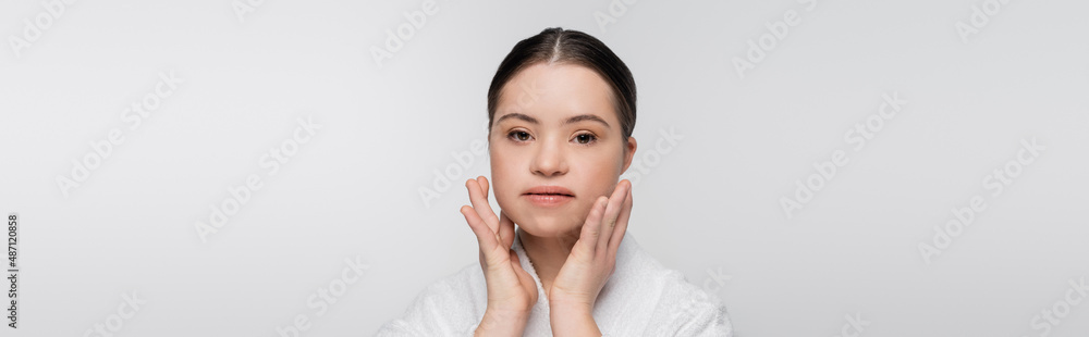 Young model with down syndrome in bathrobe touching face isolated on grey, banner Young model with down syndrome in bathrobe touching face isolated on grey, banner