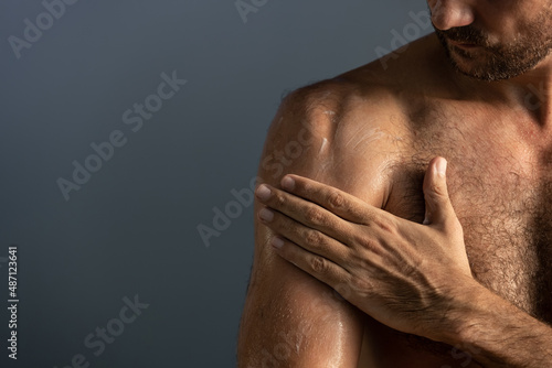Close up of handsome masculine man applying cream or moisturizing body lotion onto body in bathroom. Selfcare and wellness