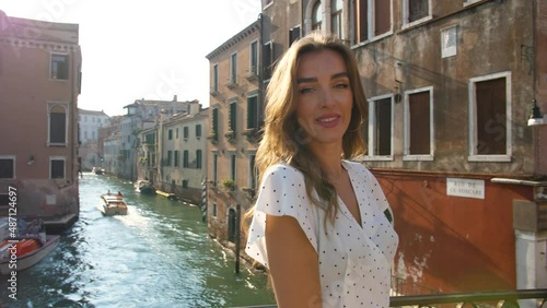 a girl in a white dress to the point, turns, looks at the camera, then to the side, standing on the bridge of the river channel in Venice