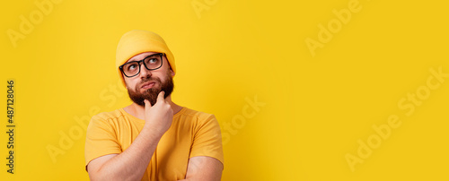 thinking bearded man looking up over yellow background, panoramic layout