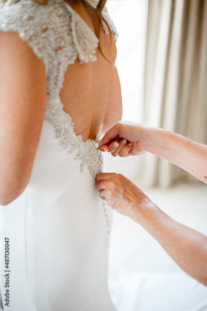 Fastens a button on the back of the bride on a white corset of a lace dress Close up Back view of the bridesmaid helps in the morning 