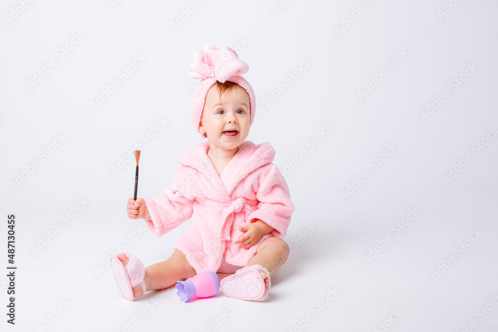 Cute little baby girl in pink terry with makeup isolated on a white background, repeats the behavior of mom Cute little baby girl in pink terry with makeup isolated on a white background, repeats the behavior of mom
