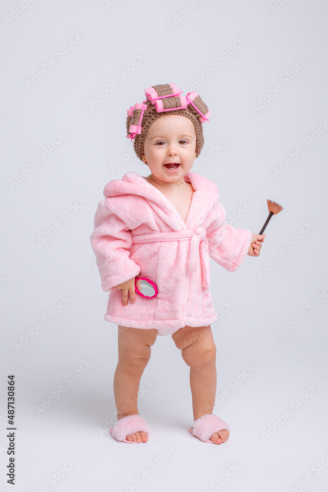 Cute little baby girl in pink terry with makeup isolated on a white background, repeats the behavior of mom Cute little baby girl in pink terry with makeup isolated on a white background, repeats the behavior of mom