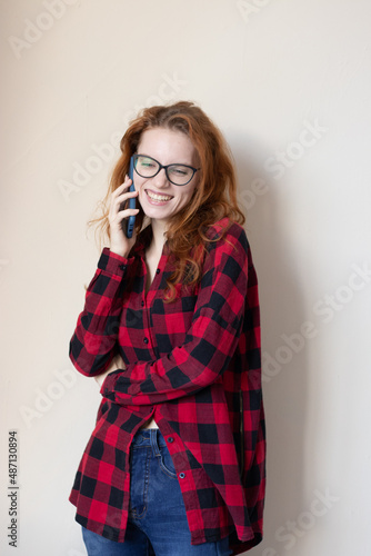 young red-haired girl talking on the phone on a light background