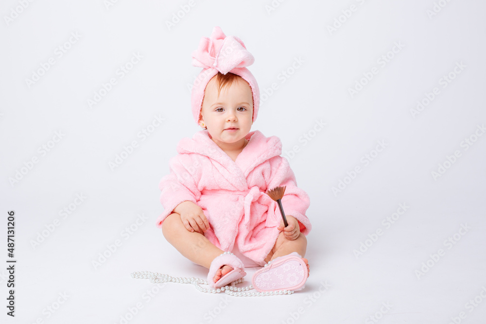 Cute little baby girl in pink terry with makeup isolated on a white background, repeats the behavior of mom Cute little baby girl in pink terry with makeup isolated on a white background, repeats the behavior of mom