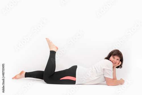 Portrait of cheerful young girl with curvy figure lying on white background after sports workout.