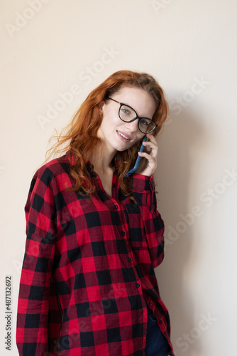 young red-haired girl talking on the phone on a light background