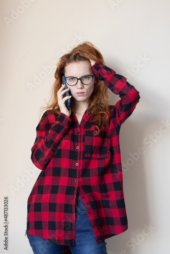 young red-haired girl talking on the phone on a light background