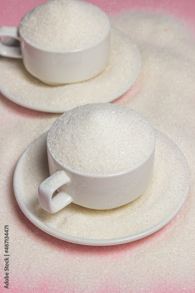 Overflowing cups with sugar on a pink background. Excessive sugar intake Overflowing cups with sugar on a pink background. Excessive sugar intake