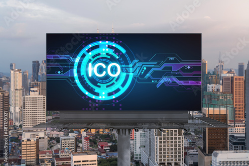 ICO hologram icon on billboard over panorama city view of Kuala Lumpur at sunset. KL is the hub of blockchain projects in Malaysia, Asia. The concept of initial coin offering, decentralized finance