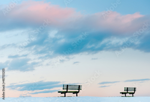 Two benches on a snow-covered glade against the backdrop of a gentle sunset sky. Minimalism. 