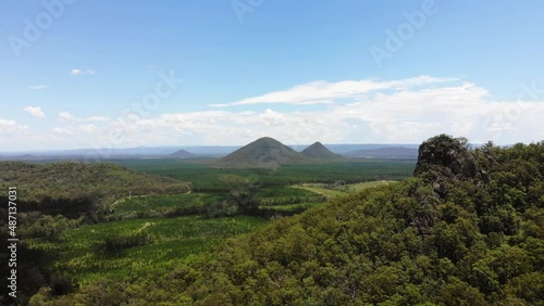 The tip of a small mountains passes by right of frame as a gorgeous group of mountains sit on the horizon, protruding out of the Earth, surrounded by young trees under the beautiful blue skies photo