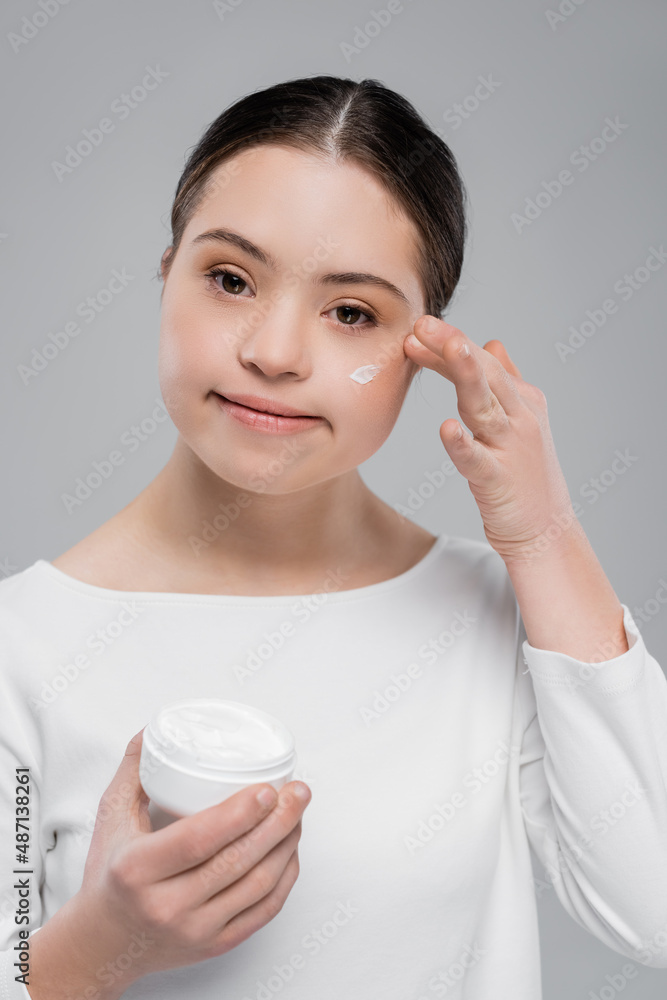 Young woman with down syndrome applying face cream isolated on grey Young woman with down syndrome applying face cream isolated on grey