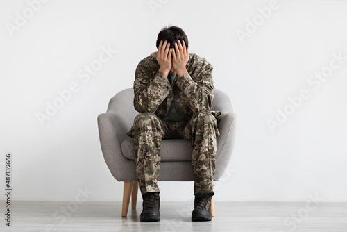 Unhappy man in camouflage sitting at arm chair, copy space © Prostock-studio