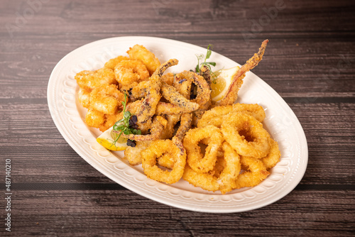 Plate with fried food made of calamari and shrimps. Delicious seafood photography against wooden table.