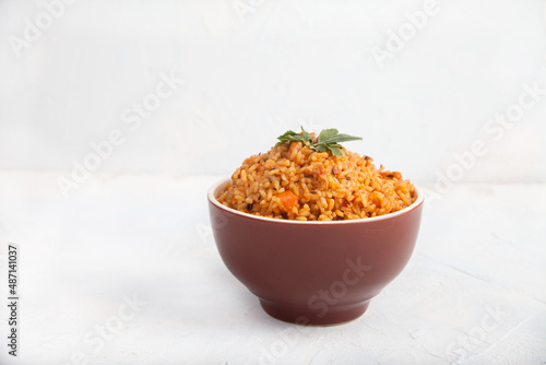 Jollof rice with parsley in a ceramic cup on a white background. National cuisine of Africa. Copy spaes.