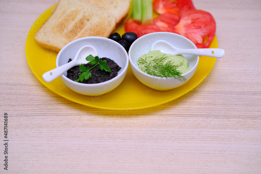 Close up of healthy breakfast with toasts, avocado dip, olive paste, tomatoes and cucumbers Close up of healthy breakfast with toasts, avocado dip, olive paste, tomatoes and cucumbers