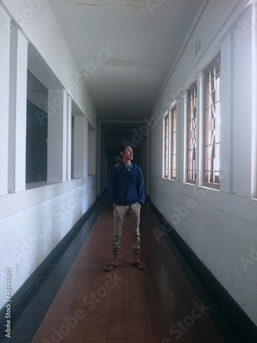 man standing alone in quiet hallway with white walls and brown floor