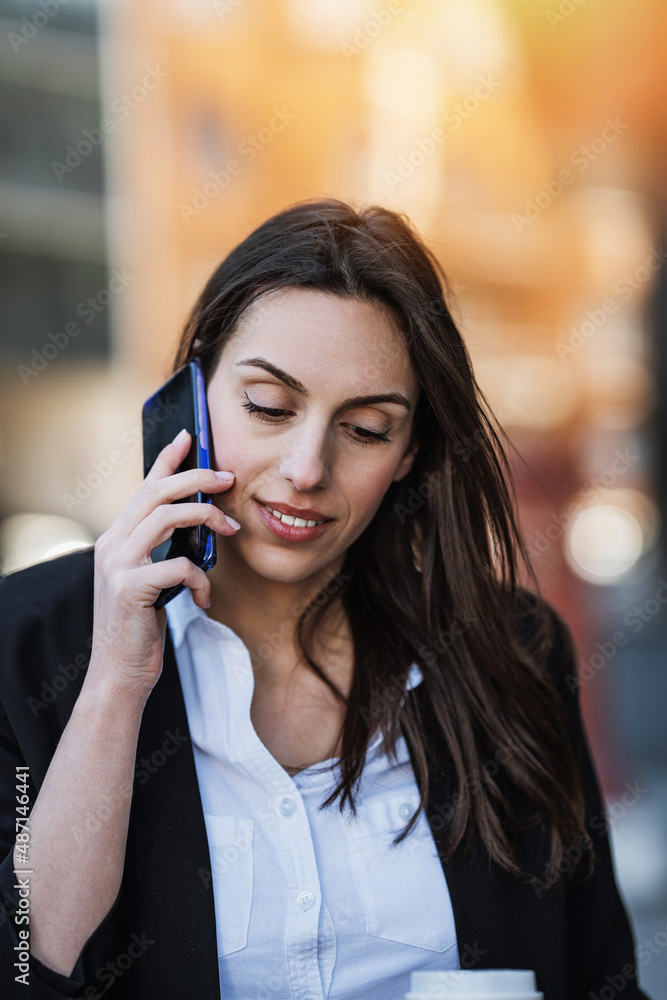 Casually dressed business woman standing on city street and using her smart phone to communicate with someone. Bright sunny day and beautiful bokeh in the background. Casually dressed business woman standing on city street and using her smart phone to communicate with someone. Bright sunny day and beautiful bokeh in the background.