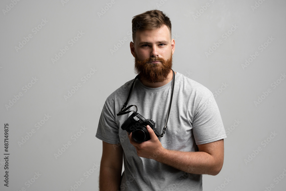 Portrait of bearded professional photographer with dslr camera looks straight into the camera isolated on gray background. Portrait of bearded professional photographer with dslr camera looks straight into the camera isolated on gray background.