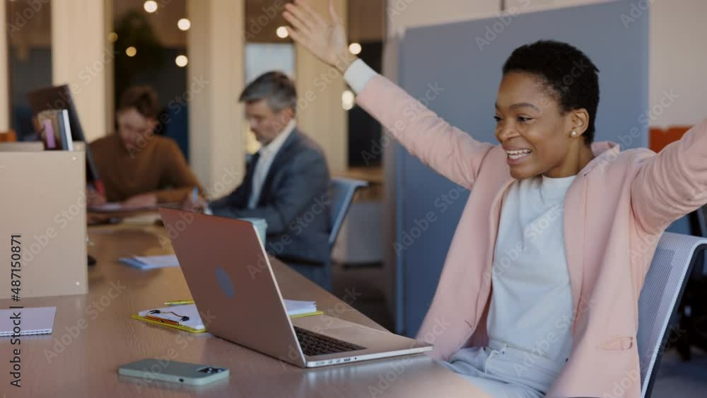 Young multiracial female office worker rejoicing of something while looking at her modern laptop. African girl sitting at the office and working. Young multiracial female office worker rejoicing of something while looking at her modern laptop. African girl sitting at the office and working.