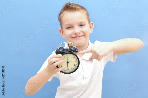 a boy on a blue background with glasses holds an alarm clock in his hands. He woke up, he has a lot of energy