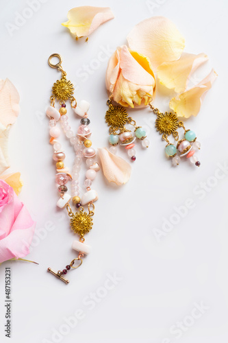 golden handmade jewerly bracelet and earning with semiprecious and roses petals at white background. hobby and life style concept