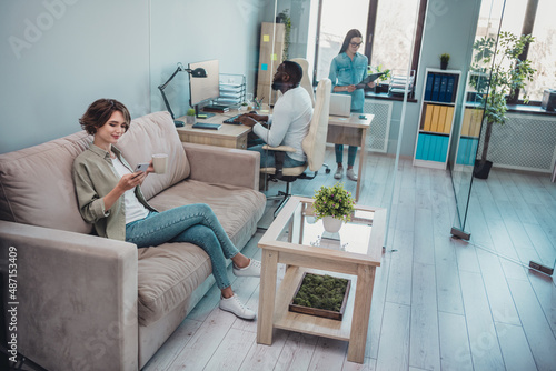 Photo of happy positive advisors sitting table having pause typing device drinking tea smiling indoors workplace workstation