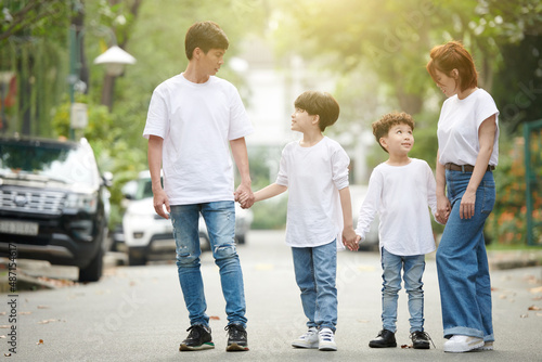 Mother and father holding hands of their kids when they are walking in the street together on sunny day