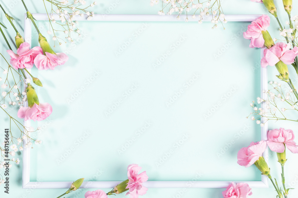 White frame with pink carnations and white gypsophila flowers on light blue. Mother's day. Mock up.