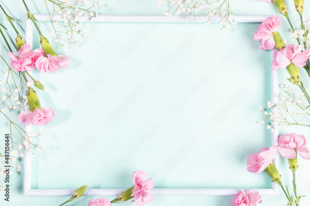 White frame with pink carnations and white gypsophila flowers on light blue. Mother's day. Mock up. White frame with pink carnations and white gypsophila flowers on light blue. Mother's day. Mock up.