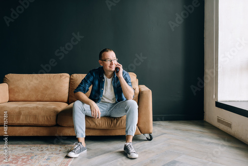 A man with glasses in casual clothes sitting on the couch smiling talking on the phone