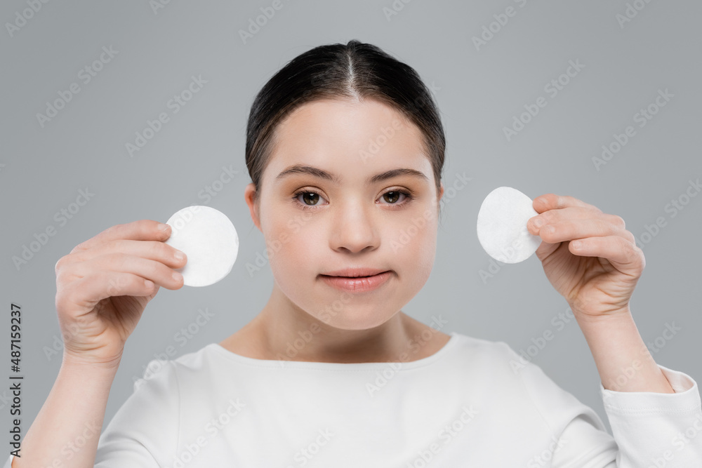 Young woman with down syndrome holding cotton pads isolated on grey