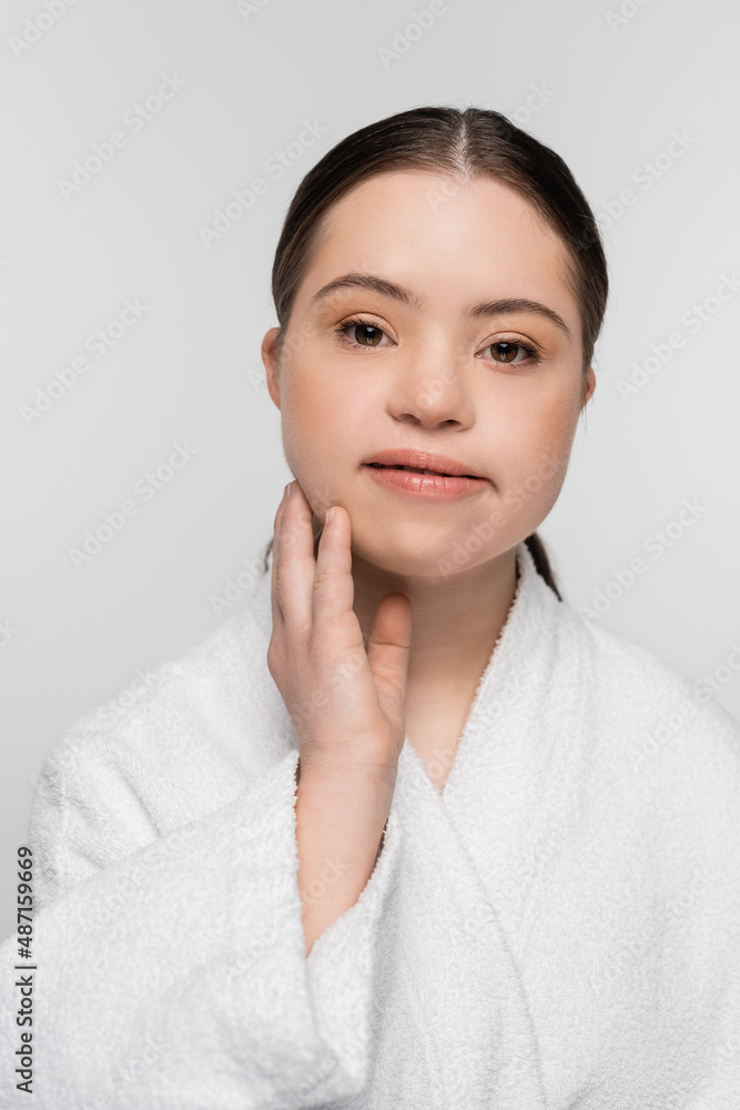 Young woman with down syndrome in bathrobe touching face isolated on grey Young woman with down syndrome in bathrobe touching face isolated on grey