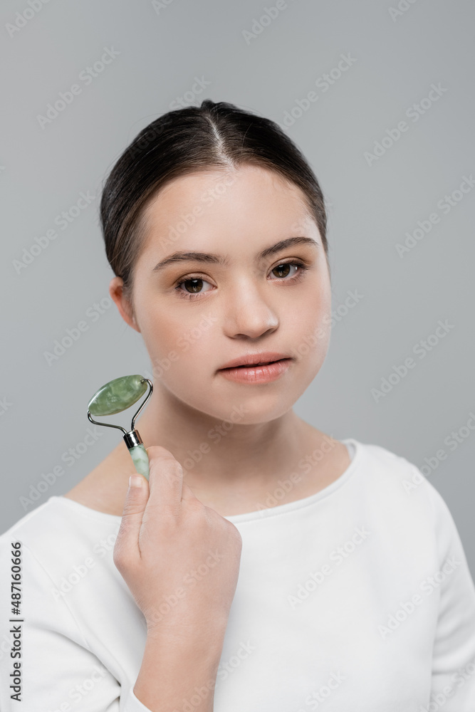 Young woman with down syndrome holding jade roller isolated on grey Young woman with down syndrome holding jade roller isolated on grey