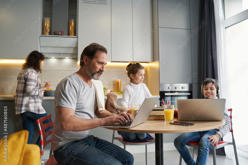 Boy and man sitting before laptops while woman cooking Boy and man sitting before laptops while woman cooking