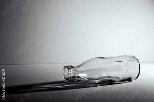 An empty glass bottle lies on the table. Copy space. Graphic still life with light and shadow in black and white colors. Concept of recyclable materials or alcoholism problems. Depressive condition