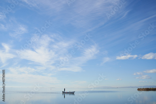 Fisherman silhouette standing on wooden fishing boat returning to port in Delta del Ebro National Park in Catalonia, symbol of traditional fishing in the delta estuary in extinction. © lensofcolors