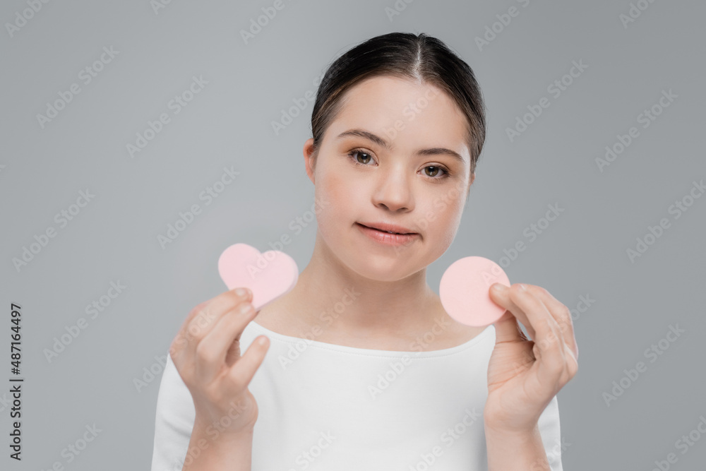 Young woman with down syndrome holding sponges isolated on grey Young woman with down syndrome holding sponges isolated on grey