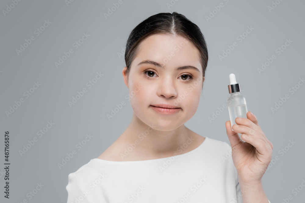 Young woman with down syndrome holding bottle of serum isolated on grey Young woman with down syndrome holding bottle of serum isolated on grey