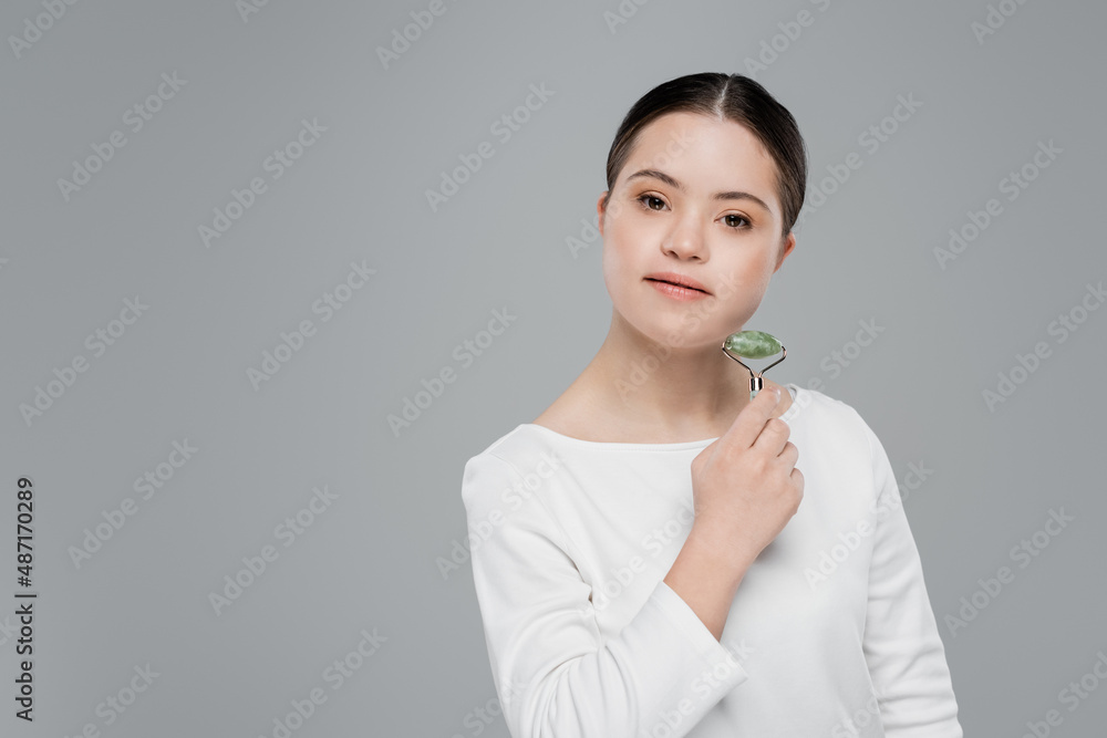 Young woman with down syndrome holding jade roller isolated on grey Young woman with down syndrome holding jade roller isolated on grey