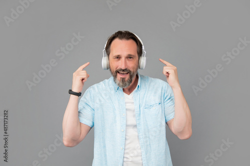 Headphones in, volume up. Happy old man point at headphones. Listening to music