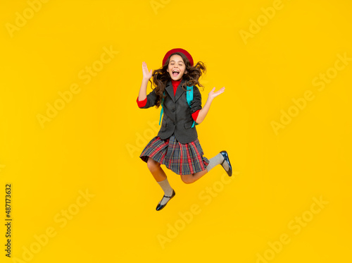glad teen girl in uniform and beret with school bag running on yellow background, schoolgirl