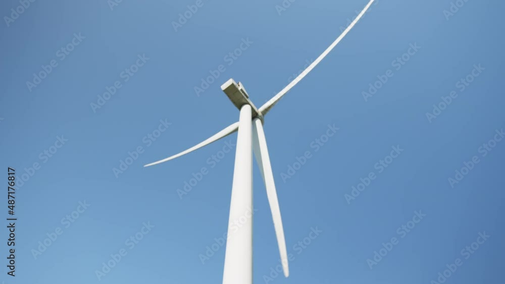 Rotating wind turbines. Green clean energy future concept. Windmill spinning with sun on blue sky. Group of windmills for electric power production. Wind propeller working on field over blue sky. Rotating wind turbines. Green clean energy future concept. Windmill spinning with sun on blue sky. Group of windmills for electric power production. Wind propeller working on field over blue sky.